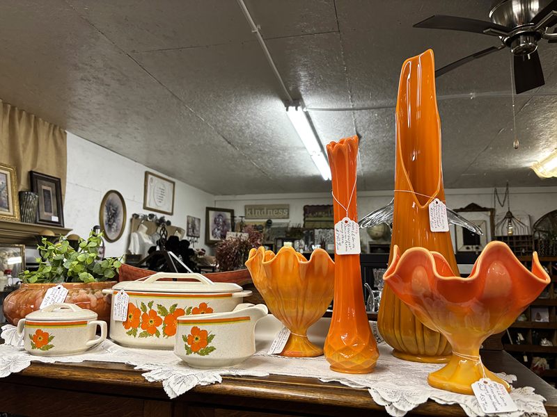 Orange glass swung vases and bowls with a poppy-pattern casserole set on a lace-covered table