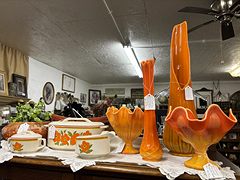 Orange glass swung vases and bowls with a poppy-pattern casserole set on a lace-covered table