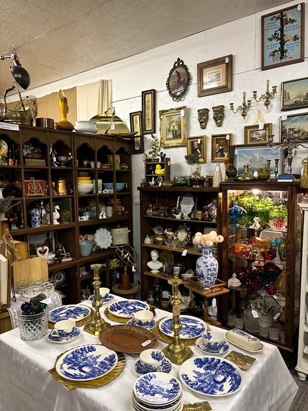 Blue-and-white china on a table in front of wooden hutches filled with antiques