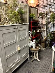 Gray painted cabinet topped with greenery next to a small white plant stand