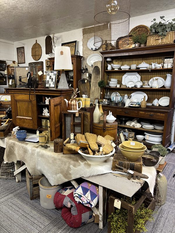 Rustic furniture with a hutch of white dishes, a hide-covered table, baskets and pottery