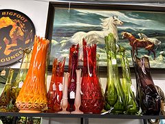 Orange, red, green and amber glass vases in front of a painting of white horses