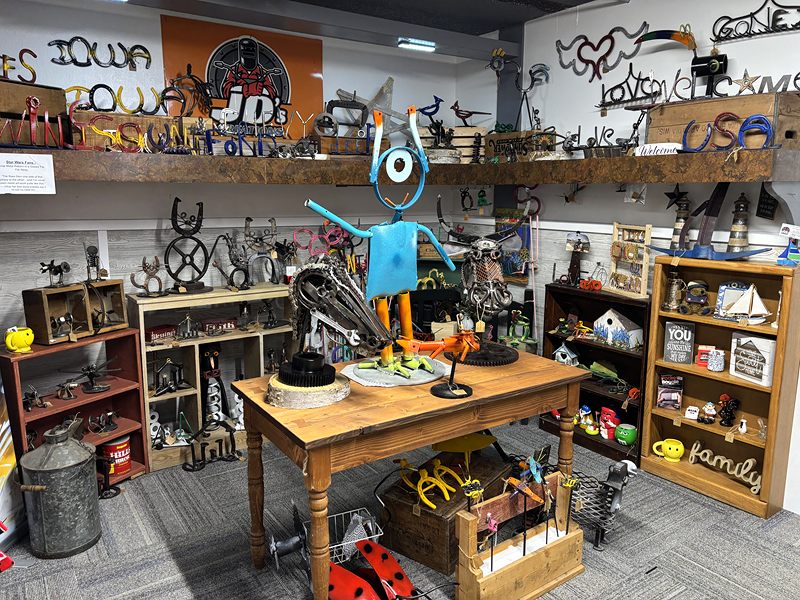 Scrap-metal yard art, including a blue robot figure on a wooden table, surrounded by metal sculptures