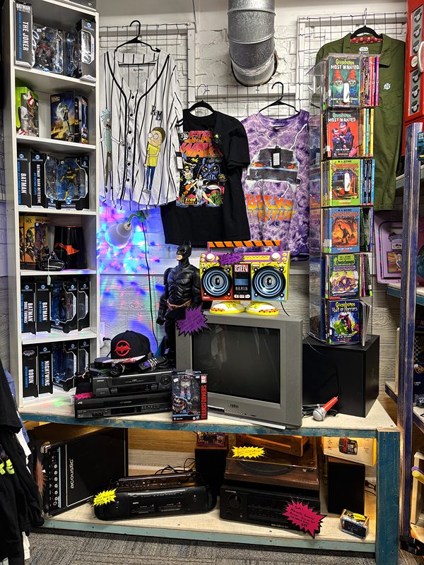 Booth of band T-shirts, action figures and electronics under colorful lights