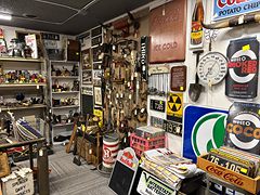 Wall of old tools and advertising signs, including Coca-Cola, above shelves of collectibles