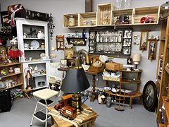 Booth with white shelves of china and figurines, a black-shaded lamp and a wooden toy truck
