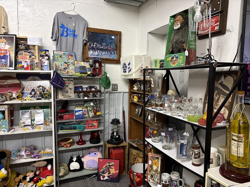 Shelves of vintage toys, plush animals and collectible glasses, with a boxed Bigfoot figure on top