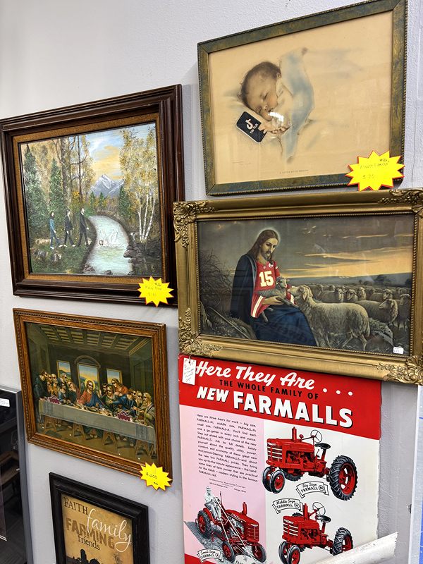 Framed vintage paintings and prints beside a red Farmall tractor advertisement