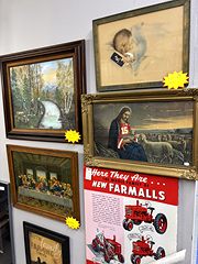 Framed vintage paintings and prints beside a red Farmall tractor advertisement