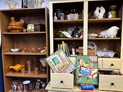 Wooden shelves with a hen-on-nest dish, amber glassware, a white rooster and vintage puzzles